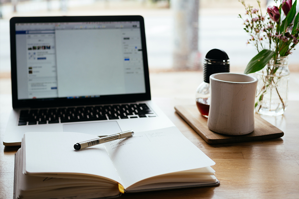 Notebook on desk near open book and tea mug