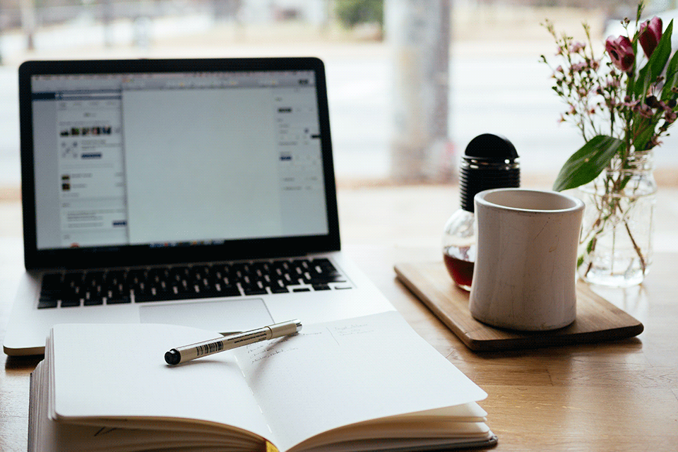 Notebook on desk near open book and tea mug